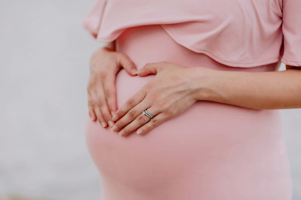 Pregnant women holding stomach with her hands that form the shape of a heart